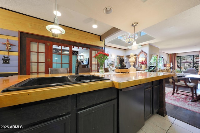 kitchen with dark cabinets, light tile patterned floors, decorative light fixtures, wooden walls, and open floor plan