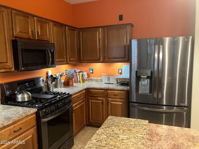 kitchen with stainless steel fridge with ice dispenser, gas stove, light stone counters, and light tile patterned floors