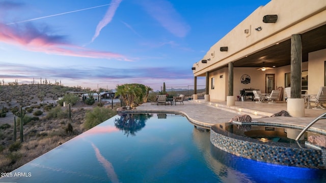 pool at dusk featuring an in ground hot tub, ceiling fan, and a patio area