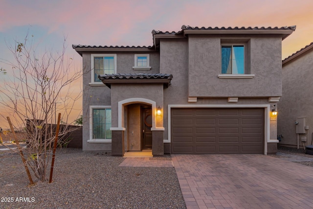 mediterranean / spanish home featuring a garage, decorative driveway, a tile roof, and stucco siding