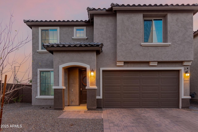 mediterranean / spanish-style house with a garage, decorative driveway, a tile roof, and stucco siding