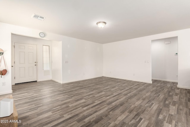 empty room featuring dark wood-type flooring, visible vents, and baseboards