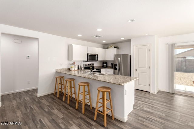 kitchen featuring appliances with stainless steel finishes, a breakfast bar area, a peninsula, light stone countertops, and white cabinetry