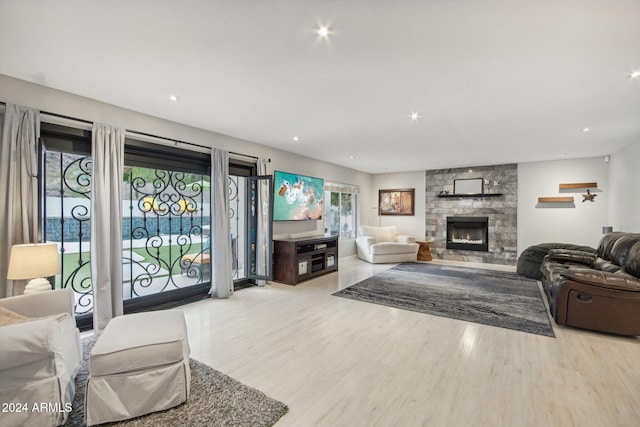 living room featuring a stone fireplace, light hardwood / wood-style flooring, and a healthy amount of sunlight