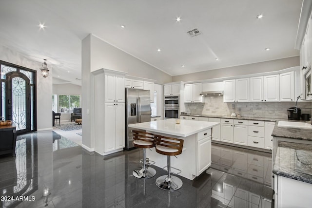 kitchen with white cabinets, vaulted ceiling, decorative backsplash, a kitchen island, and appliances with stainless steel finishes