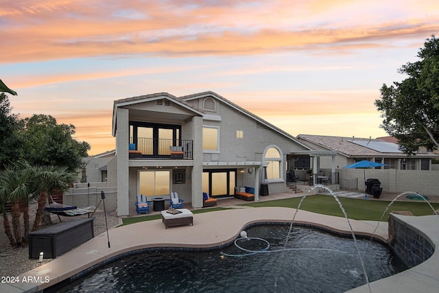 back house at dusk featuring an outdoor living space, pool water feature, a balcony, and a fenced in pool