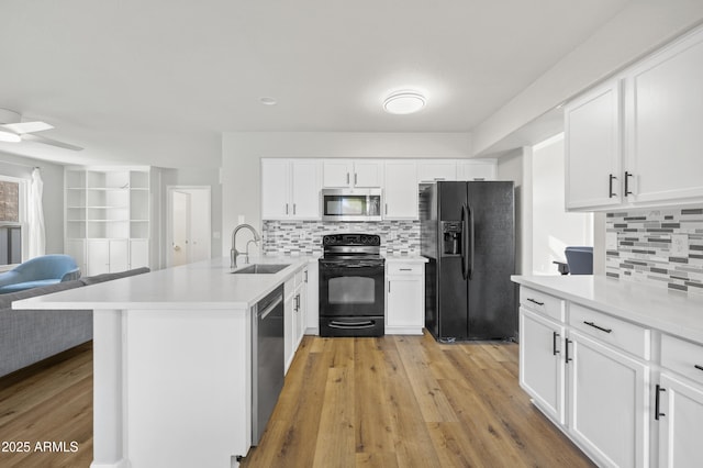 kitchen with light wood finished floors, open floor plan, a sink, a peninsula, and black appliances