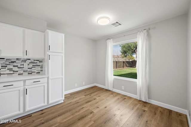 unfurnished dining area featuring baseboards, visible vents, and light wood finished floors