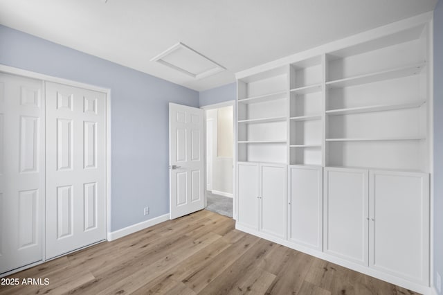 unfurnished bedroom featuring a closet, wood finished floors, attic access, and baseboards