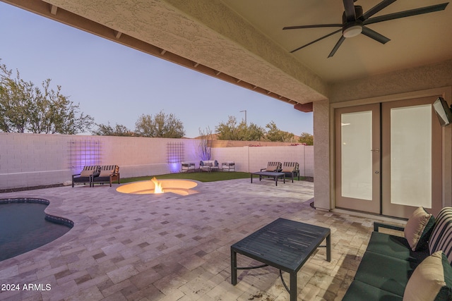 patio terrace at dusk with ceiling fan, an outdoor living space with a fire pit, and french doors