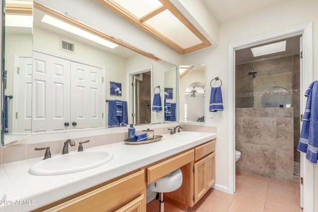 bathroom with a tile shower, vanity, ceiling fan, toilet, and tile patterned floors