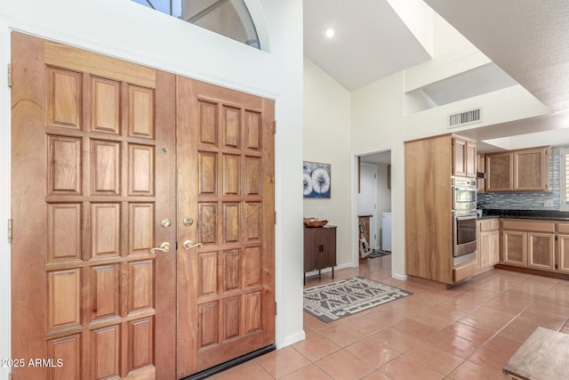 kitchen featuring stainless steel double oven, high vaulted ceiling, decorative backsplash, and light tile patterned floors