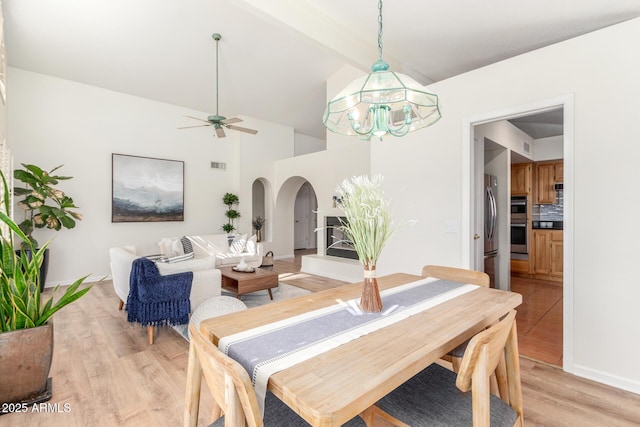 dining room with ceiling fan with notable chandelier, light hardwood / wood-style flooring, and lofted ceiling with beams