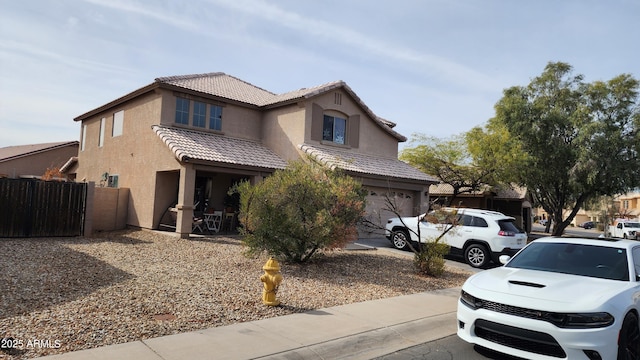 traditional-style home with driveway, a tiled roof, an attached garage, fence, and stucco siding