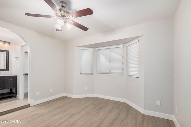 spare room with arched walkways, light wood-type flooring, a ceiling fan, and baseboards