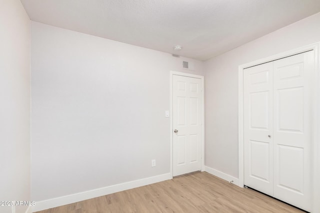 unfurnished bedroom with light wood finished floors, baseboards, and a closet