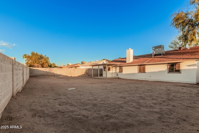 rear view of property with a fenced backyard, a chimney, cooling unit, and stucco siding