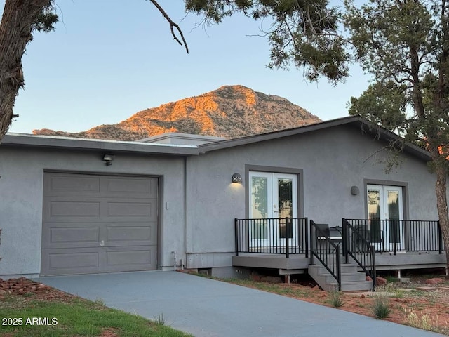 ranch-style home with driveway, a mountain view, stucco siding, french doors, and a garage
