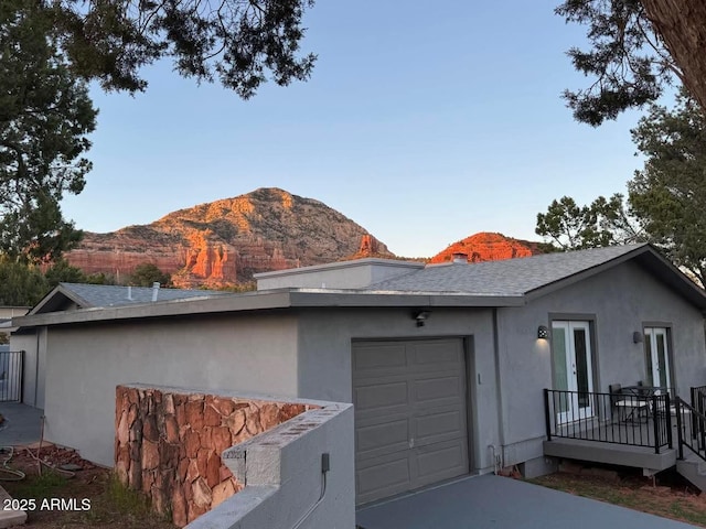 view of home's exterior featuring driveway, a shingled roof, a mountain view, an attached garage, and stucco siding