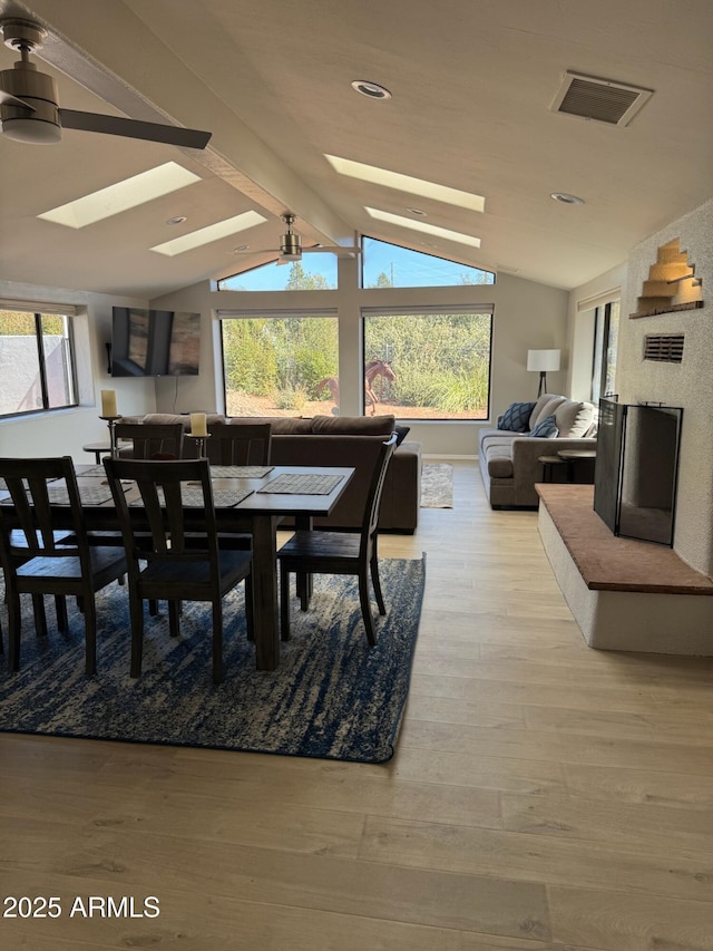 dining space with visible vents, a healthy amount of sunlight, vaulted ceiling with skylight, and light wood-style floors