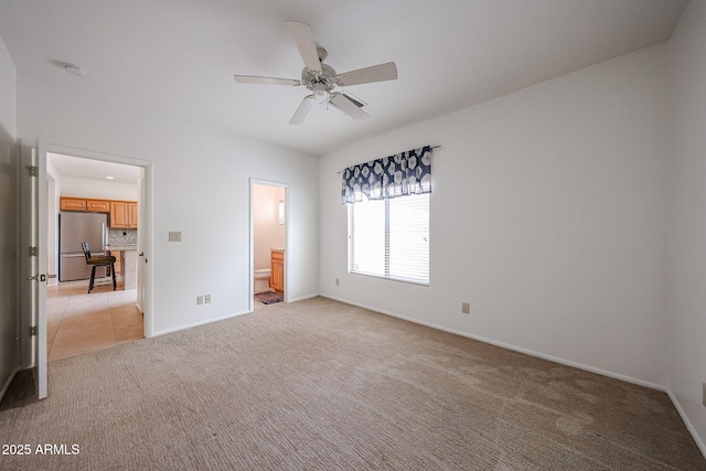 unfurnished bedroom featuring freestanding refrigerator, light carpet, baseboards, and ensuite bath