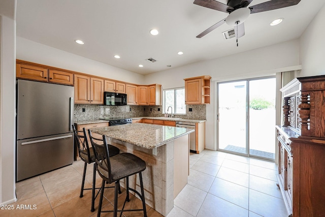 kitchen with black appliances, a sink, backsplash, a kitchen island, and light stone counters