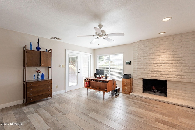 office space featuring a textured ceiling, light wood finished floors, a brick fireplace, and visible vents