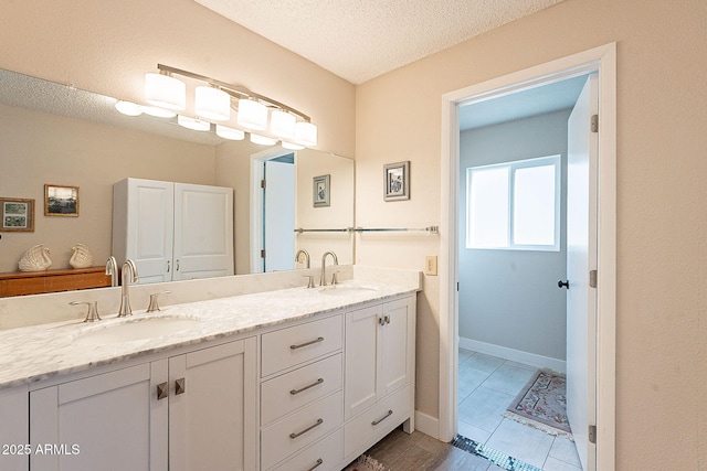 bathroom with a sink, a textured ceiling, baseboards, and double vanity