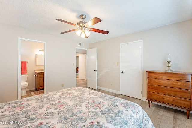 bedroom featuring a textured ceiling, ceiling fan, ensuite bathroom, baseboards, and light wood-type flooring