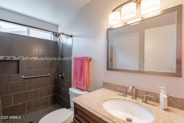 bathroom featuring tiled shower, a textured wall, vanity, and toilet