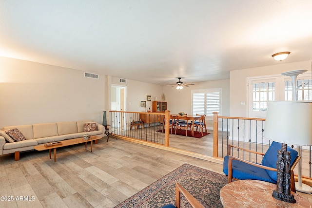 living room featuring light wood-style flooring, visible vents, and ceiling fan