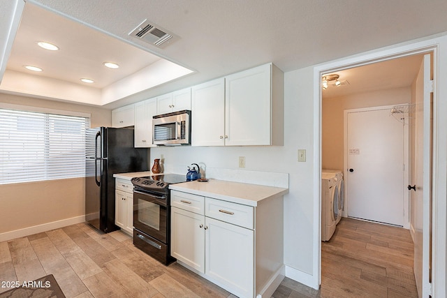 kitchen featuring a tray ceiling, visible vents, light wood-style flooring, separate washer and dryer, and black appliances