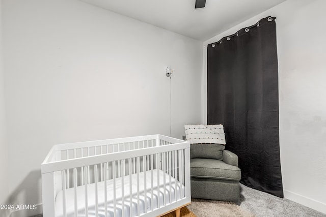 carpeted bedroom featuring a nursery area, a ceiling fan, and baseboards