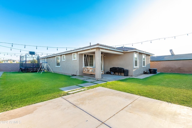 back of house featuring a patio, a trampoline, a fenced backyard, and a yard