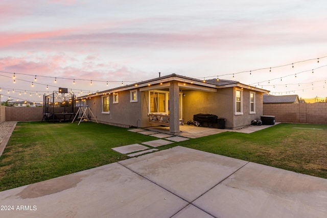 back of property with a trampoline, stucco siding, a fenced backyard, a yard, and a patio area