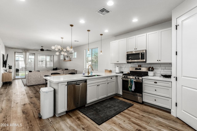 kitchen with wood finished floors, visible vents, a peninsula, a sink, and stainless steel appliances