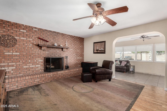 living area with a brick fireplace, a ceiling fan, and tile patterned flooring