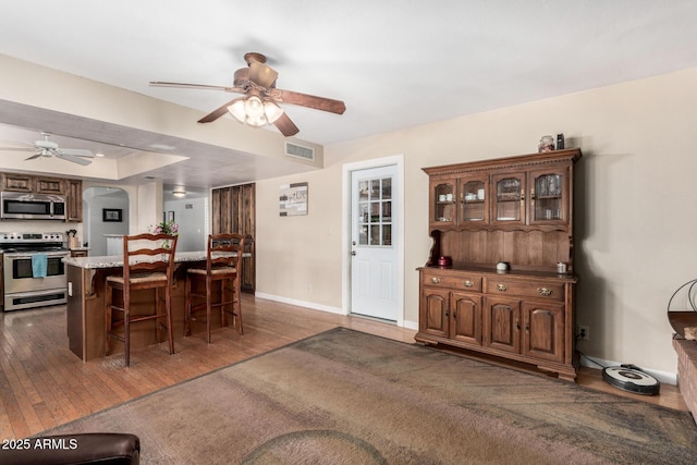 dining space with dark wood-style floors, baseboards, visible vents, a tray ceiling, and ceiling fan