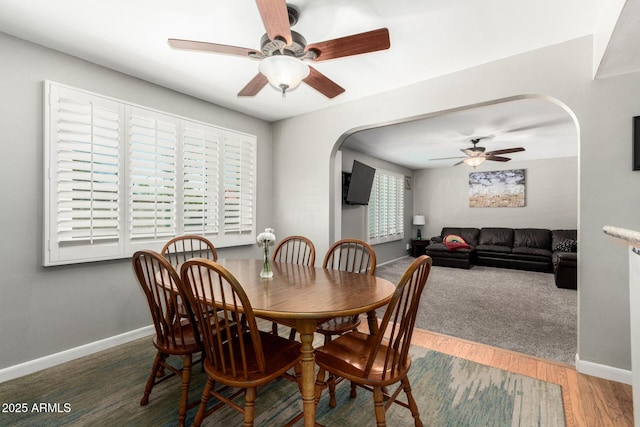 dining area with arched walkways, a ceiling fan, baseboards, and wood finished floors