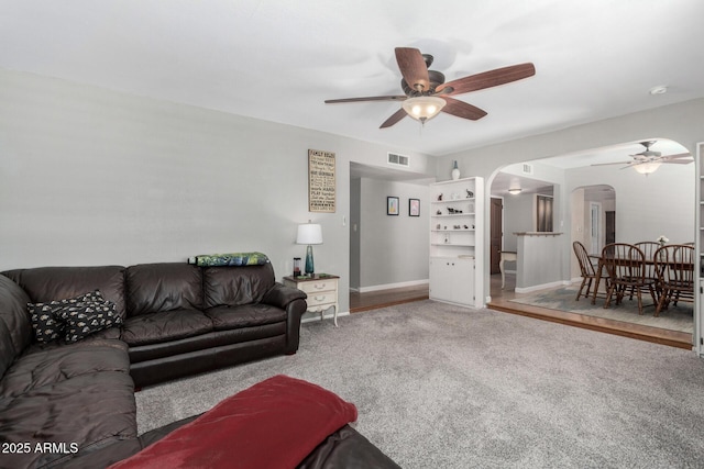 carpeted living room with arched walkways, visible vents, baseboards, and a ceiling fan