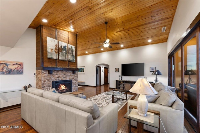 living room featuring a towering ceiling, dark hardwood / wood-style floors, a fireplace, ceiling fan, and wooden ceiling