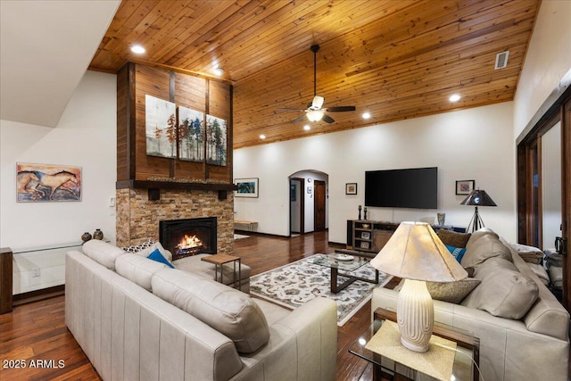 living room featuring a towering ceiling, a fireplace, dark hardwood / wood-style flooring, ceiling fan, and wooden ceiling