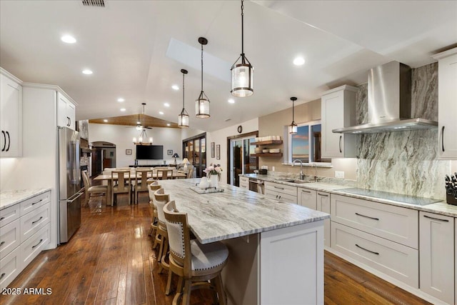 kitchen featuring appliances with stainless steel finishes, pendant lighting, sink, a kitchen bar, and wall chimney range hood