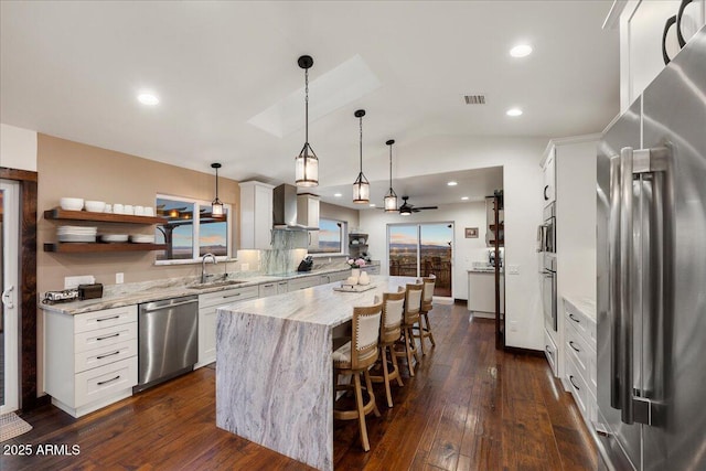 kitchen featuring light stone counters, hanging light fixtures, a kitchen island, stainless steel appliances, and white cabinets