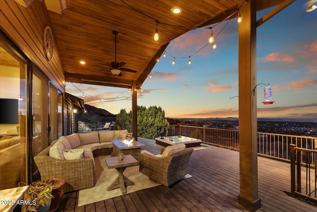 deck at dusk with ceiling fan, a jacuzzi, and an outdoor living space with a fire pit