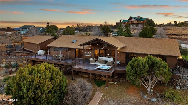 back house at dusk with an outdoor living space and a deck