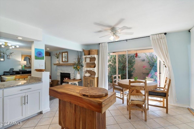 kitchen featuring white cabinetry, ceiling fan, light stone countertops, a fireplace, and light tile patterned floors