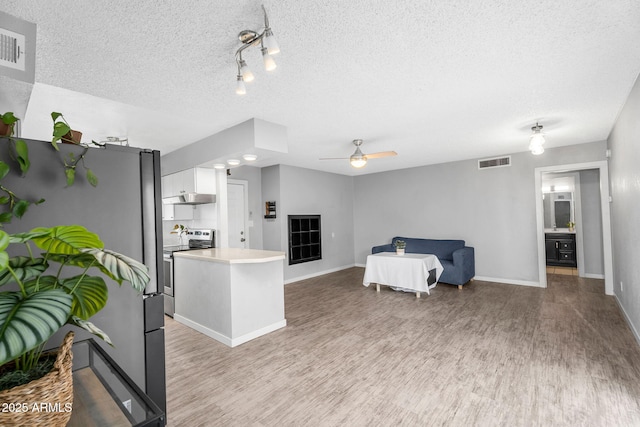 living area with a textured ceiling, light wood-type flooring, visible vents, and baseboards