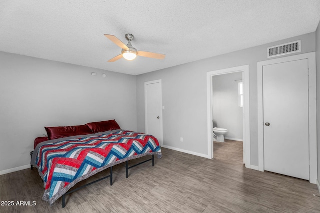 bedroom with a textured ceiling, wood finished floors, visible vents, and baseboards