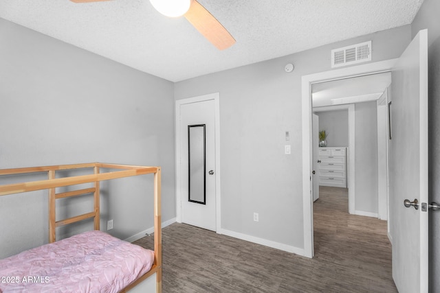 bedroom featuring baseboards, wood finished floors, visible vents, and a textured ceiling